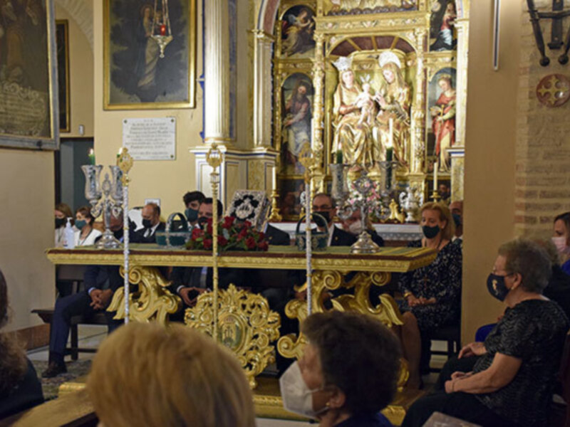 Una ceremonia religiosa en una iglesia, con una imagen central dorada y varias personas en el fondo, algunas con máscaras faciales.