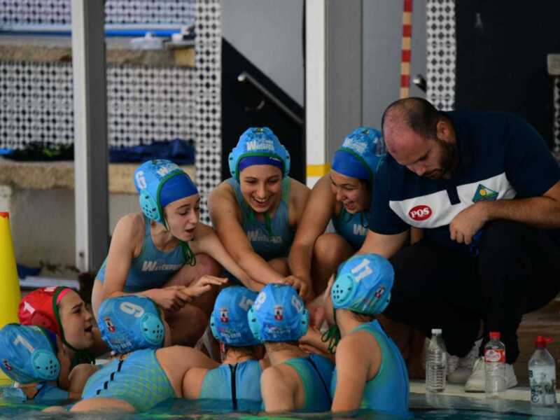 Equipo de waterpolo femenino en una reunión estratégica con su entrenador en la piscina.