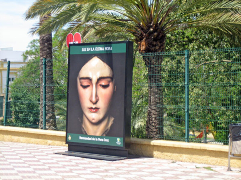 Cartel de la Virgen de la Luz en la plaza, con fondo verde y detalles de la hermandad de la Vera-Cruz.