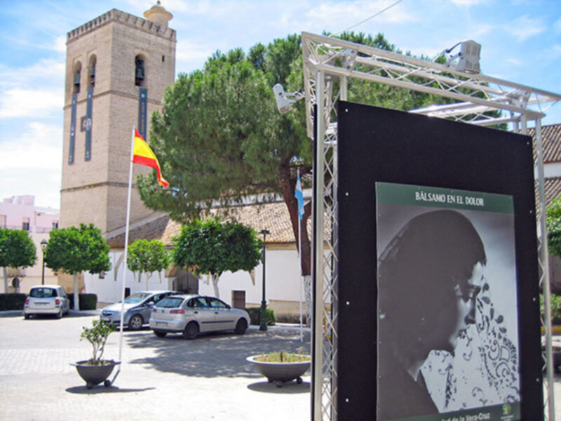 Plaza con torre de iglesia y cartel de 'Bálsamo en el Dolor' en el centro.
