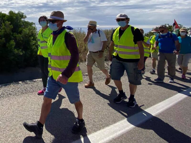 Grupo de personas caminando en una carretera, algunos con chalecos reflectantes y mascarillas, bajo un cielo parcialmente nublado.