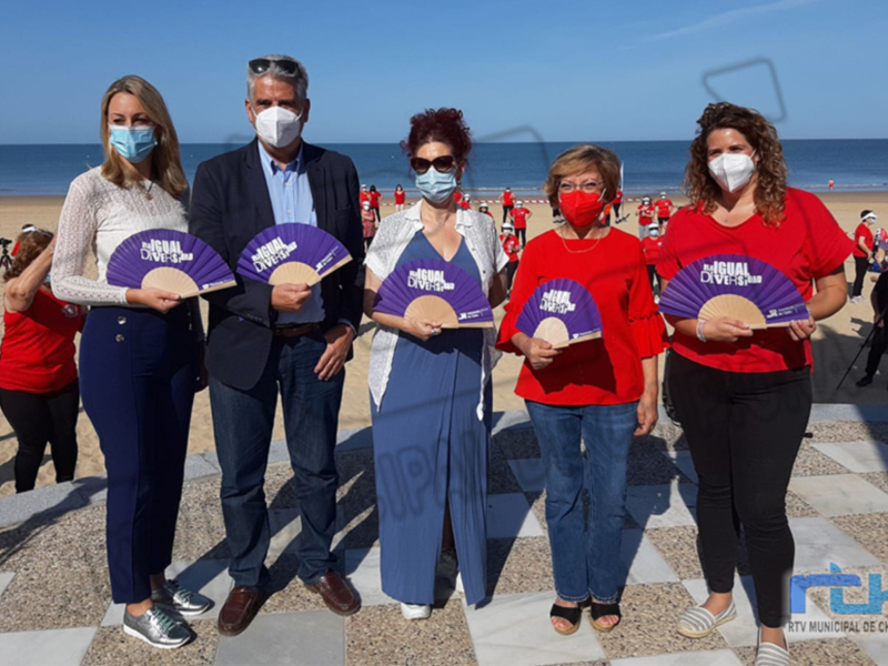 Evento en la playa con participantes sosteniendo abanicos con el texto 'Igualdad Diversidad'.