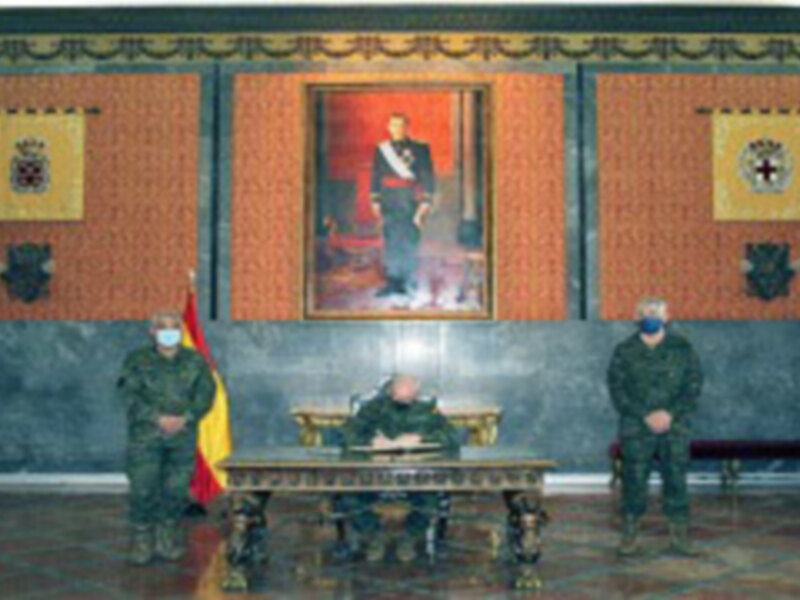 Reunión oficial en un salón decorado con un retrato central, con tres personas en uniforme militar sentadas alrededor de una mesa.