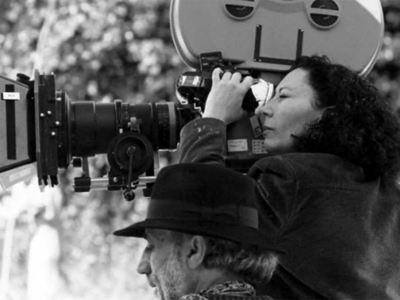 Una mujer operando una antigua cámara de filmación en blanco y negro.