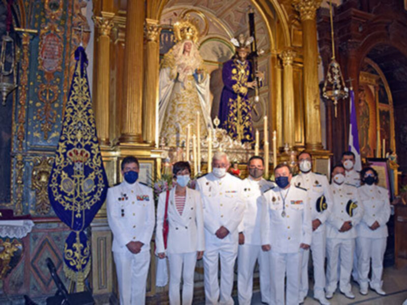 Oficiales de la Marina en uniforme blanco y máscaras faciales posan frente a una imagen religiosa en un altar ornamental.