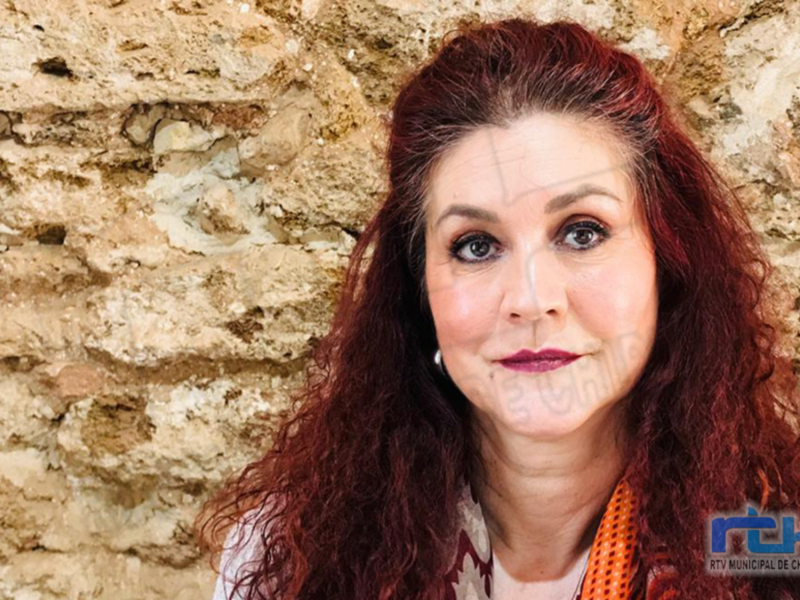 Retrato de una mujer con cabello rojo frente a un fondo de pared de piedra.