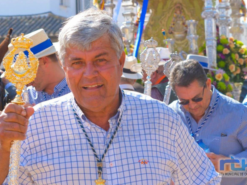 Hombre sosteniendo un cetro en una procesión religiosa, con vestimenta típica y ornamentos festivos.