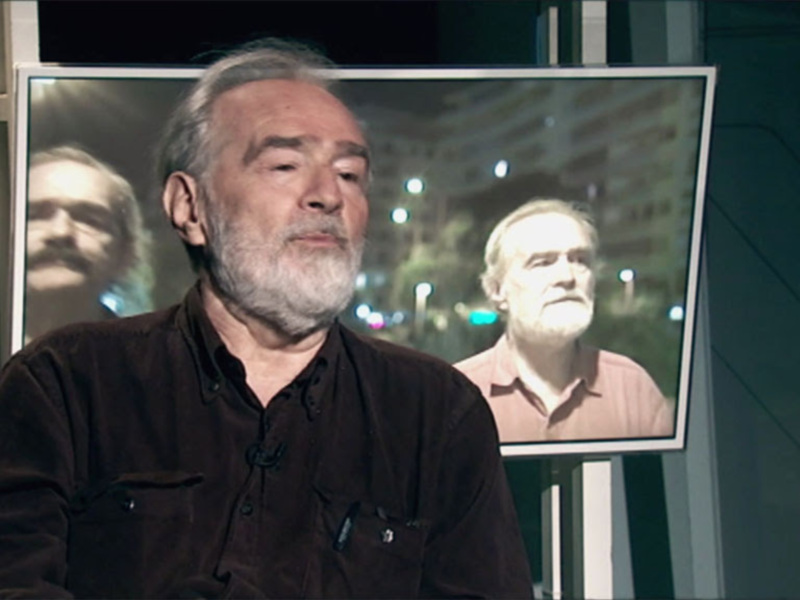 Entrevista a un hombre con una imagen de él en la pantalla de fondo.