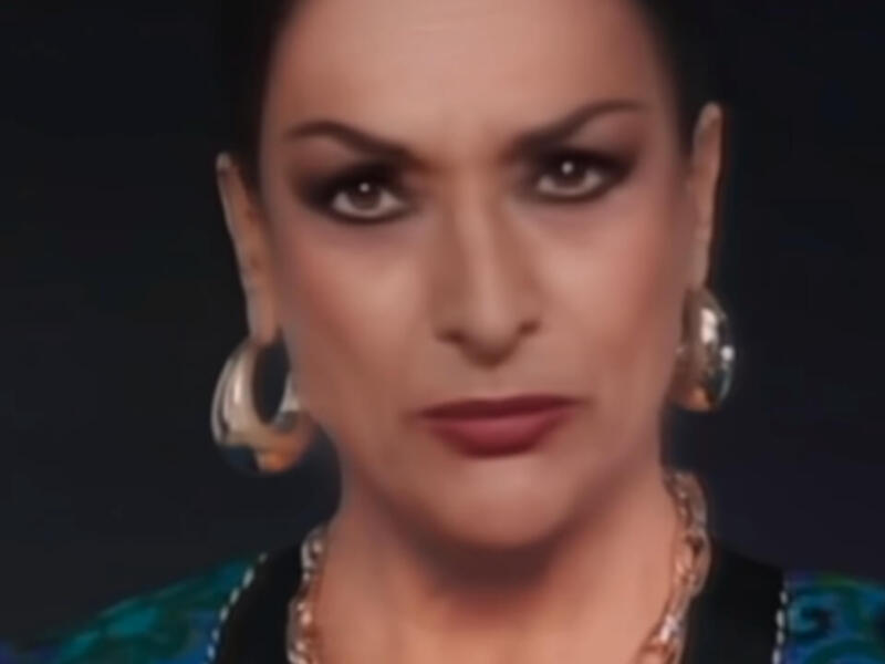 Retrato de una mujer con maquillaje dramático y joyas grandes, fondo oscuro.