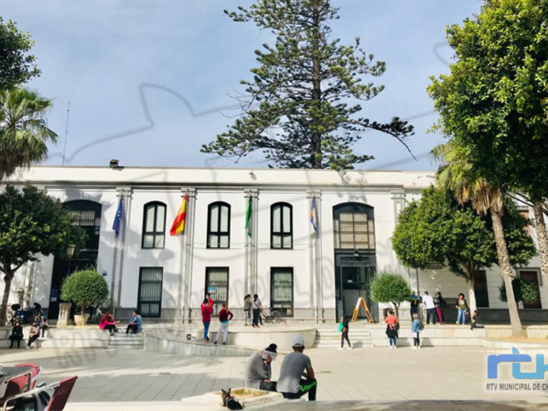 Fachada de una edificio público con banderas y personas en la plaza.