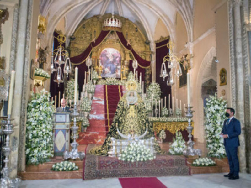 Elegante altar decorado con flores blancas y velas, con una imagen central y dos ángeles en el fondo, en un ambiente de lujo y solemnidad.