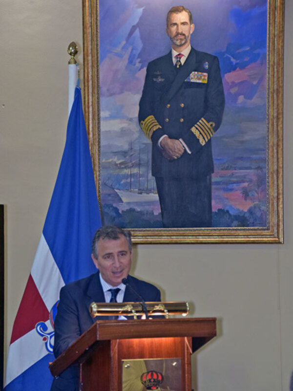 Discurso oficial en un evento con retrato de un líder militar en el fondo y bandera dominicana en la izquierda.
