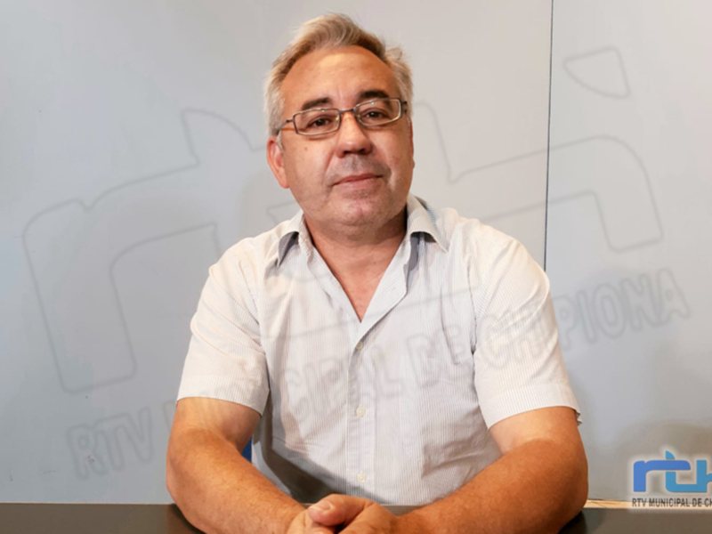 Un hombre con cabello blanco y barba, vistiendo una camisa blanca, posa frente a un fondo con la marca "RTV Municipal de Chipiona".