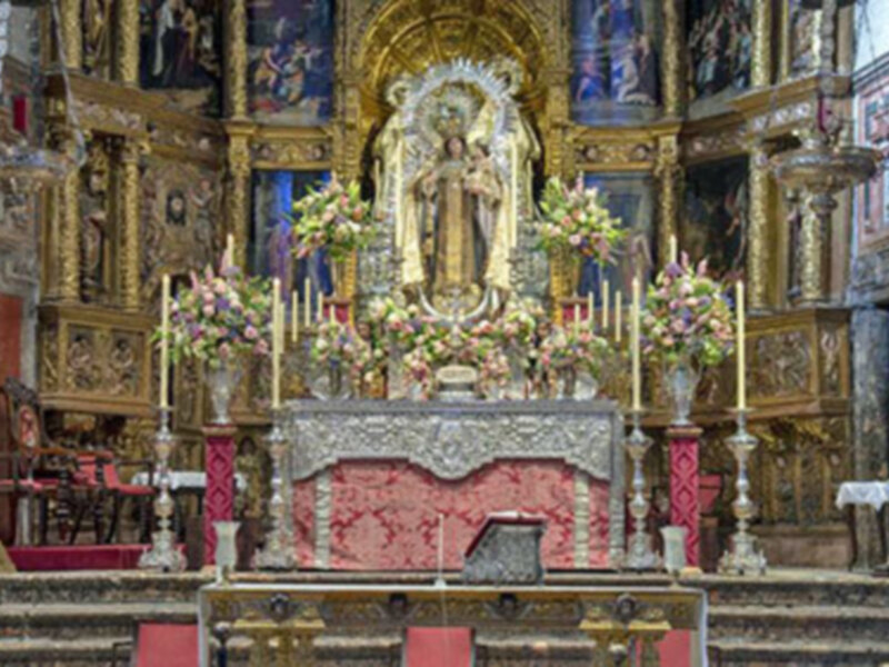 Interior de una iglesia con altar ornamental, imágenes religiosas y flores en el centro.