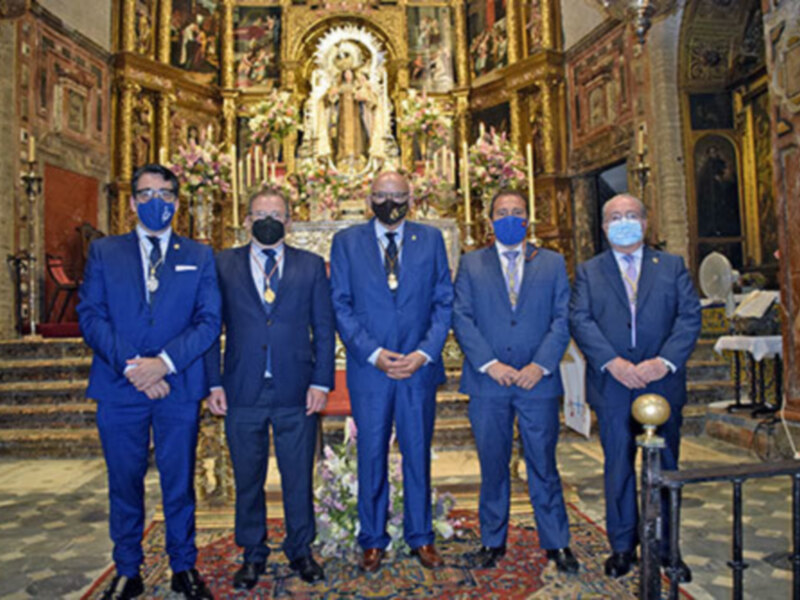 Ceremonia en el interior de una iglesia con cinco hombres en trajes y mascarillas, ante un altar ricamente decorado.