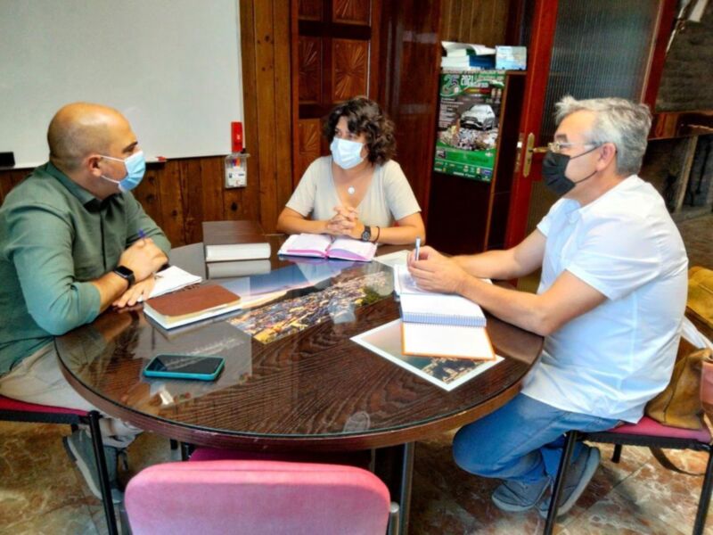 Reunión en mesa redonda con tres personas, discutiendo y tomando notas con el uso de mascarillas.