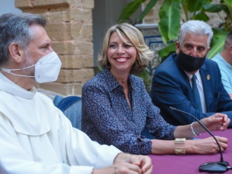 Conferencia de prensa con autoridades y una mujer sonriente en un ambiente formal, con el uso de mascarillas por precaución.