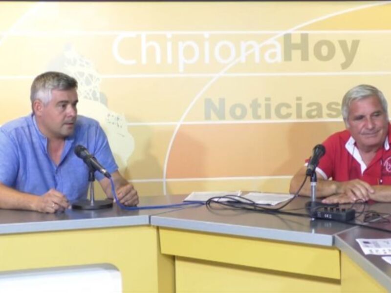 Dos hombres sentados en un estudio de radio, con micrófonos y notas en frente de ellos, en un fondo amarillo con la palabra 'Noticias' escrita.