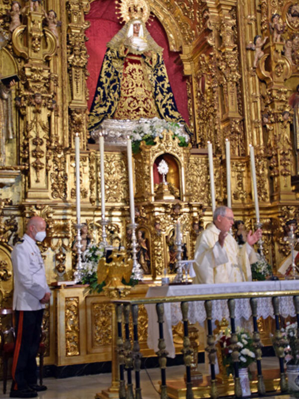 Eucaristía en un altar ornado con dorado y alta imagen religiosa, presidida por sacerdotes y un oficial en uniforme.