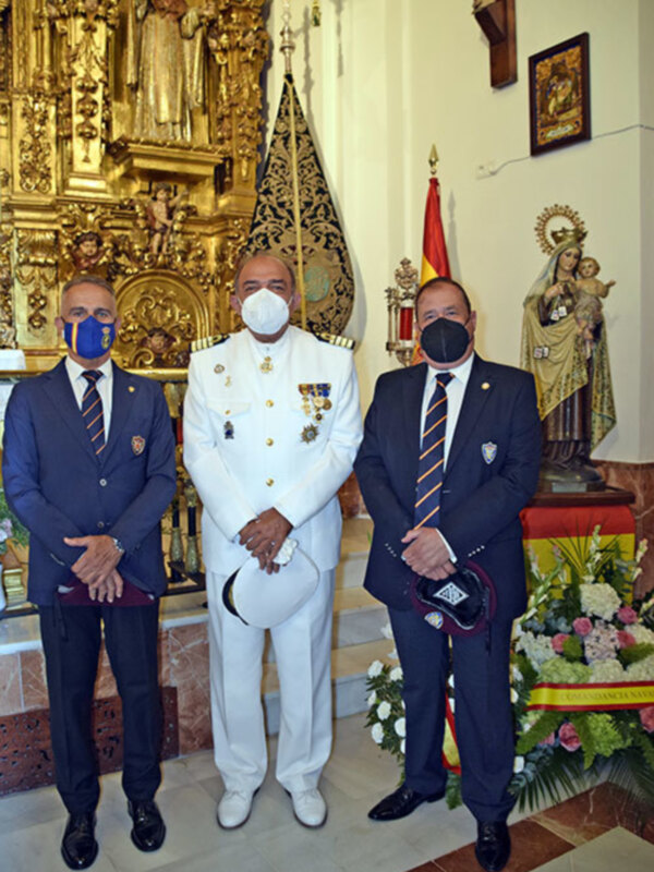 Tres hombres en trajes formales y máscaras faciales posan frente a un altar ornamental en una iglesia.