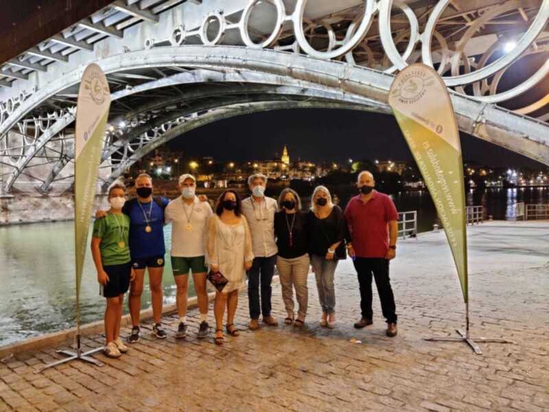 Grupo de personas posando frente a un puente iluminado en la noche, con un letrero de la Fundación León de Andalucía en el fondo.