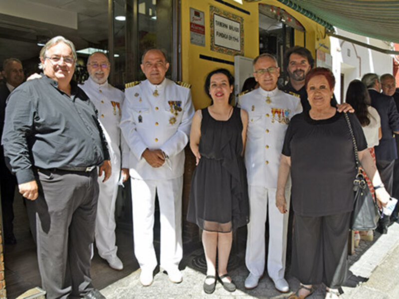 Grupo de personas en uniforme y civiles posando juntos en el exterior de una tienda.