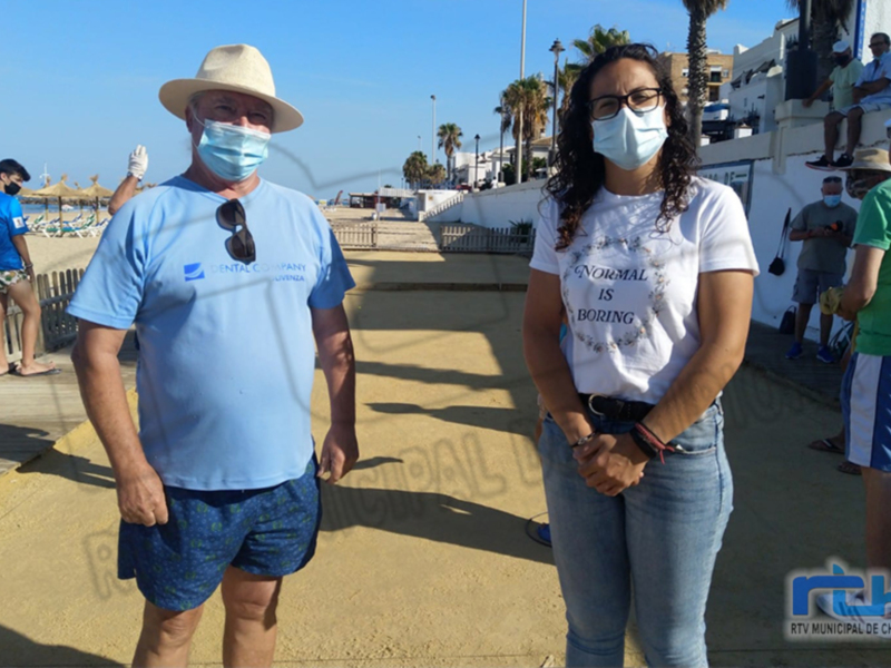 Personas con mascarillas en la playa de Chipiona, España, bajo un cielo azul claro.