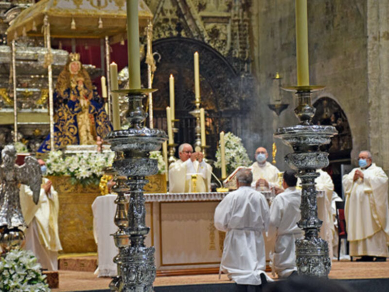 Sacerdotes en una ceremonia religiosa en un interior de iglesia con alta decoración y velas iluminando el altar.