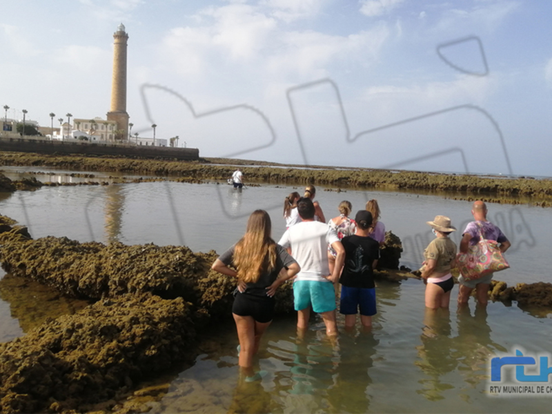 Turistas explorando las piscinas naturales junto al faro de Chipiona, España.