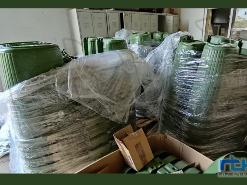 Pila de contenedores de plástico verdes en una oficina o almacén, algunos envueltos en plástico. El ambiente parece ser un lugar de almacenamiento o distribución de materiales.