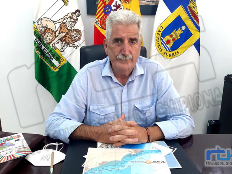 Persona sentada en una oficina con banderas y mapas, representando la administración municipal de Chipiona.