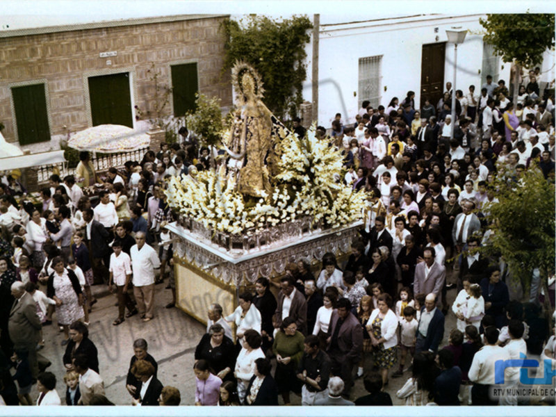 Festividad religiosa con una imagen venerada en el centro, rodeada de una multitud de personas vestidas de blanco y negro, posiblemente durante una procesión religiosa.