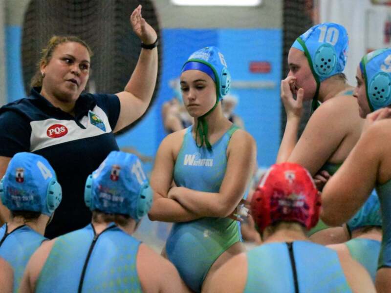 Entrenamiento de waterpolo femenino con el equipo y su entrenadora en una piscina cubierta.