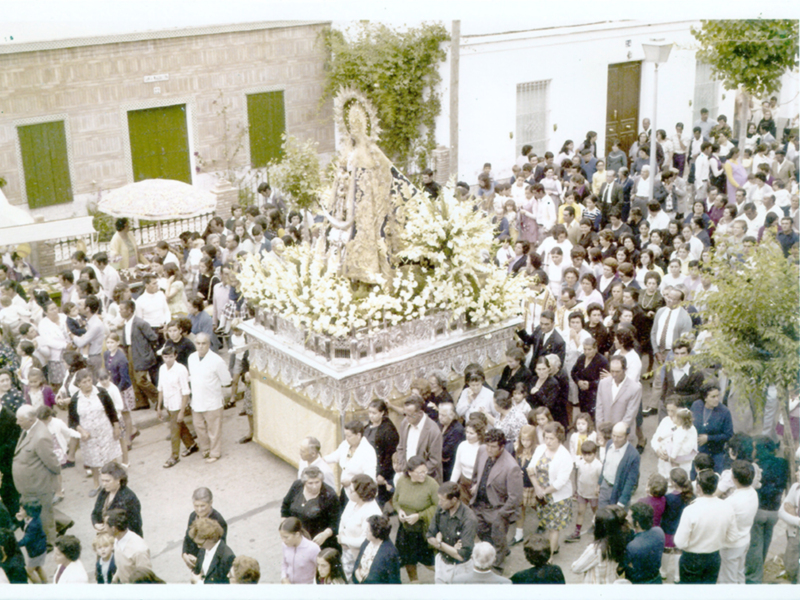 Procesión religiosa con imagen de la Virgen, acompañada por una multitud de personas en una plaza urbana.