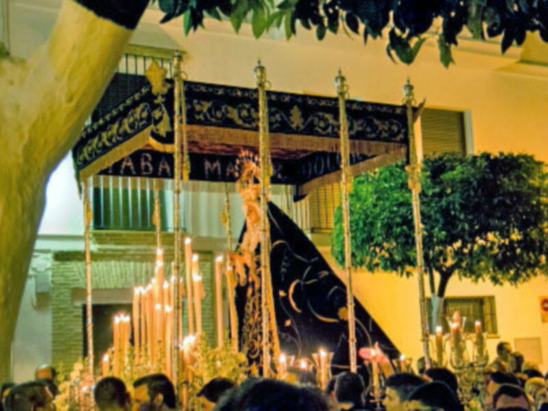 Procesión religiosa con la imagen de la Virgen María en un entorno urbano iluminado por velas y ornamentos.