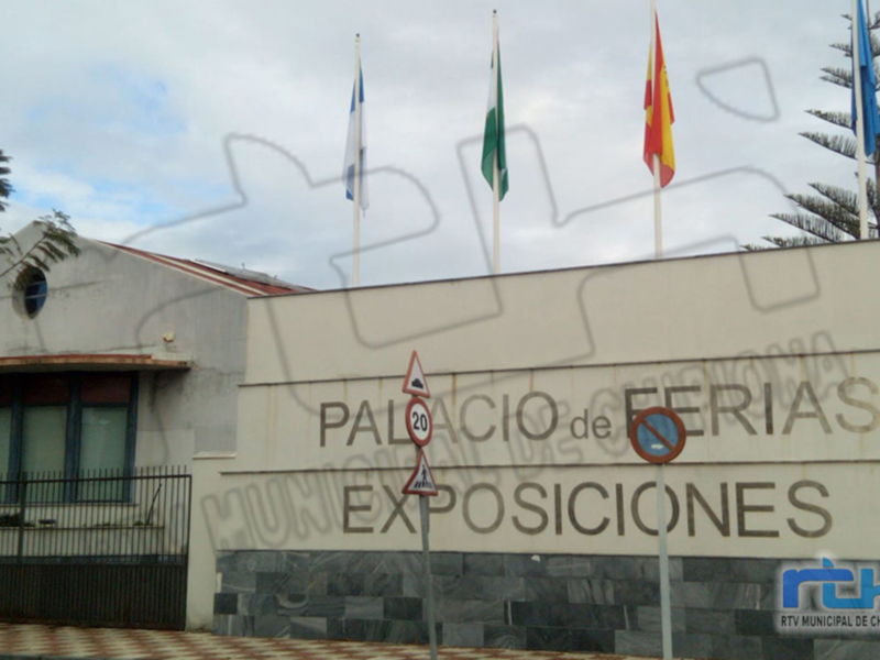 Palacio de Ferias y Exposiciones de Chipiona, con banderas y señal de tráfico en el frente.