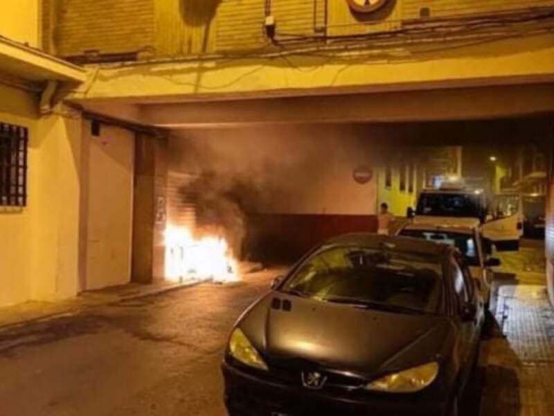 Incendio en un garaje nocturno con vehículos aparcados alrededor.