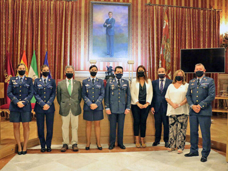 Fotografía de una ceremonia de graduación militar en un auditorio, con oficiales militares y civiles posando ante un retrato de un oficial militar.