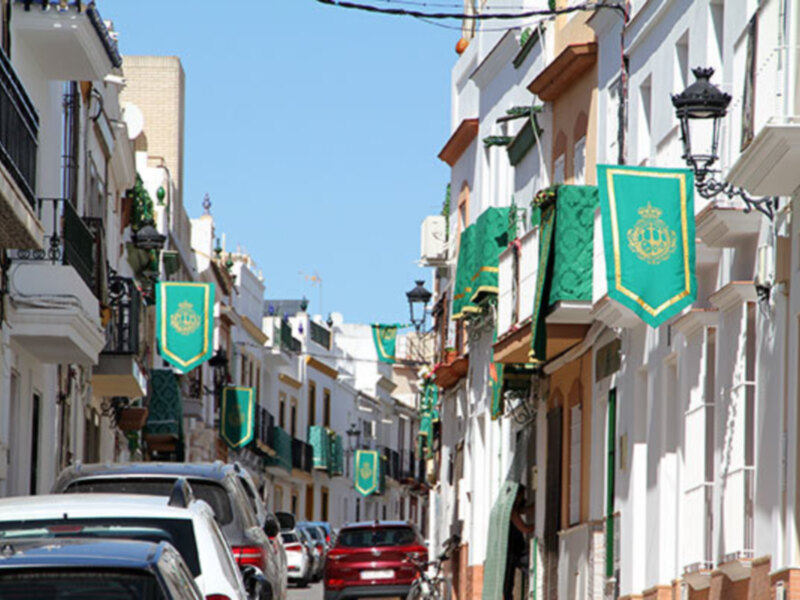 A picturesque street lined with white buildings and green banners, suggesting a European town or city.