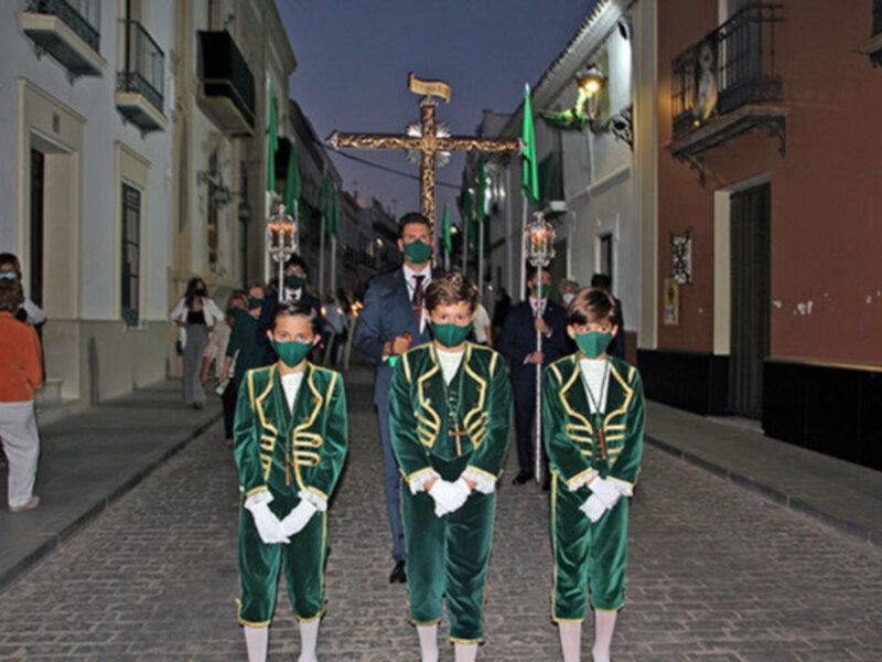 Jóvenes portando una cruz en una procesión nocturna en una calle adoquinada, con edificios históricos al fondo.