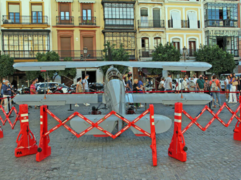 Exposición de avión en plaza histórica con barreras de seguridad y edificios antiguos al fondo.