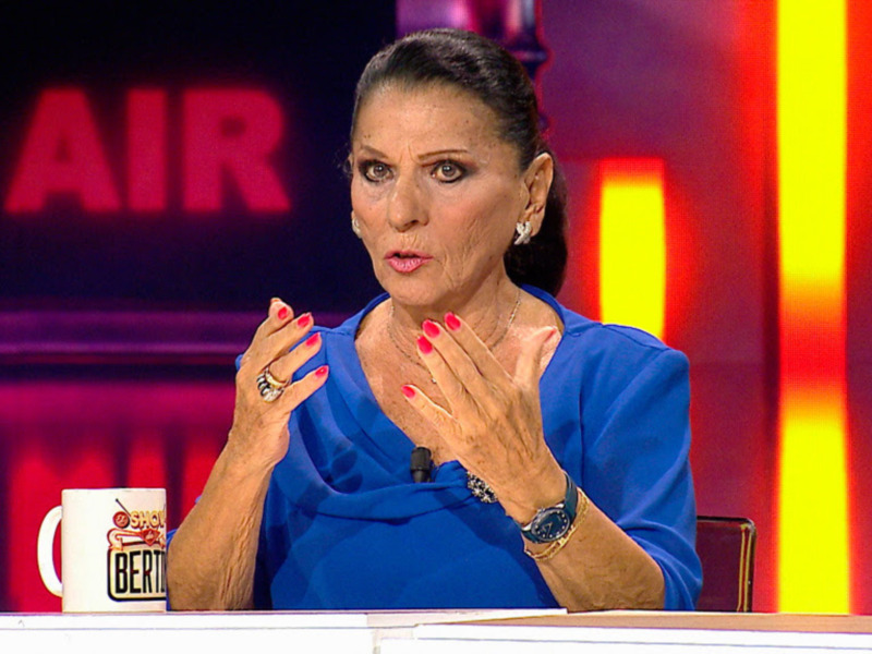 Una mujer hablando en un programa de televisión con un fondo rojo y amarillo.