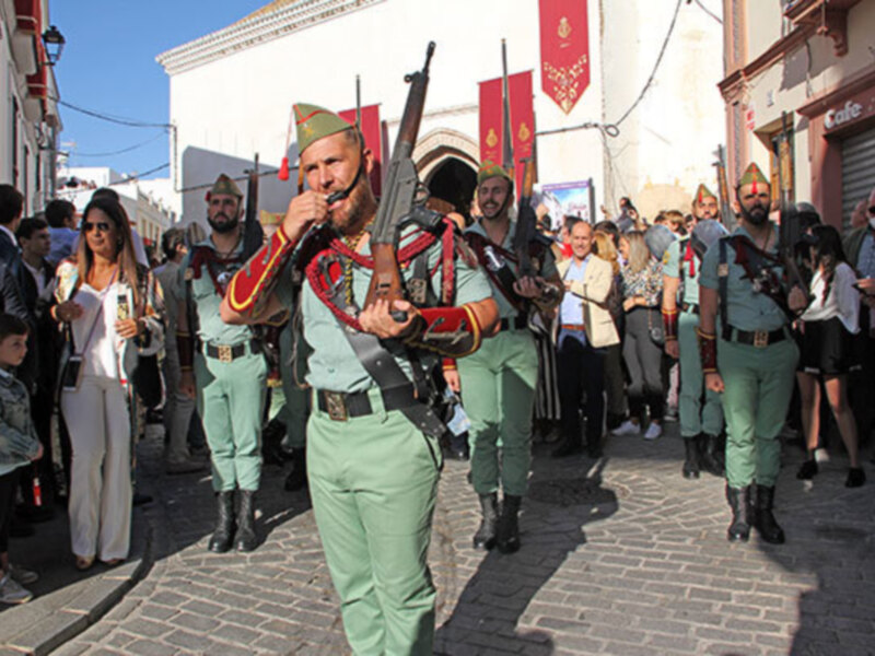 Soldado en uniforme tradicional desfilando en una calle con edificios históricos y espectadores.