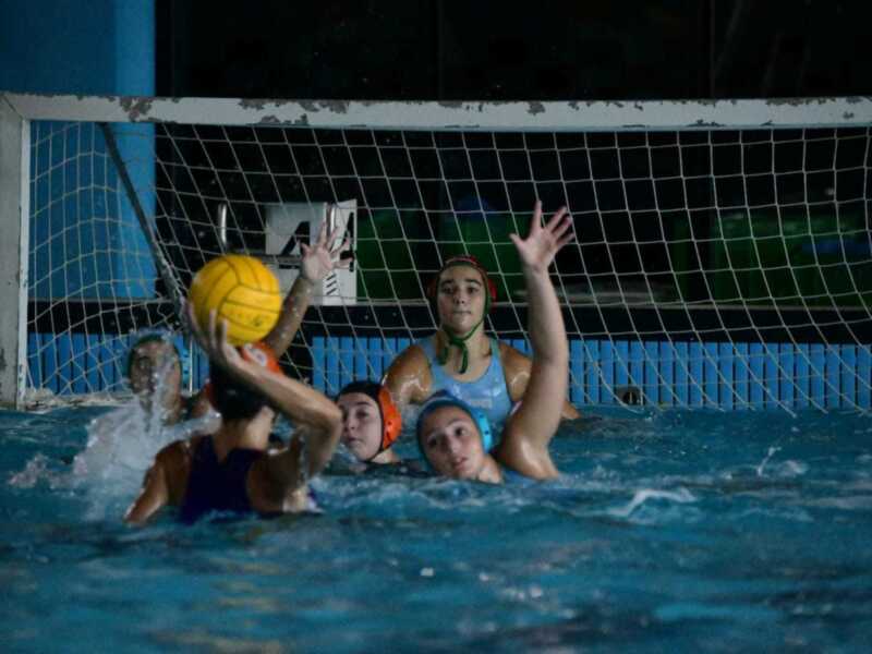 Jugadoras de waterpolo en acción durante un partido, intentando marcar un gol.