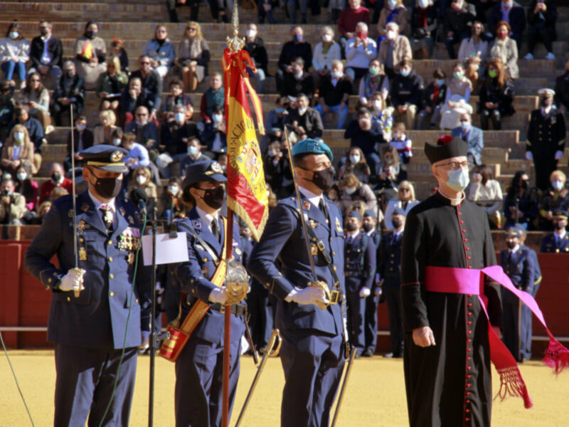 Ceremonia oficial con uniformes militares y bandera española, presenciada por un público en un anfiteatro.