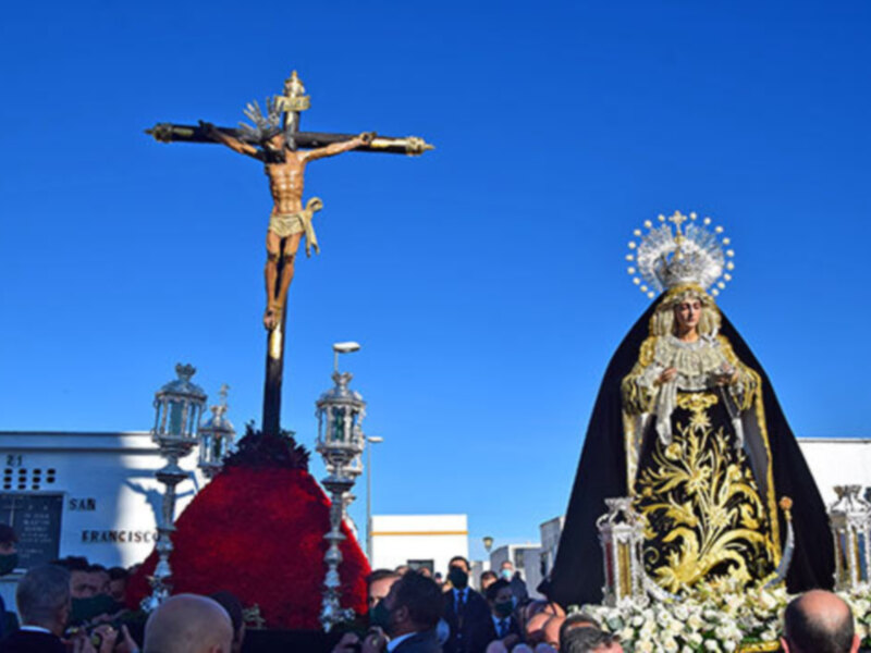 Procesión religiosa con una imagen de la Virgen María y un crucificado en el centro, bajo un cielo azul claro.