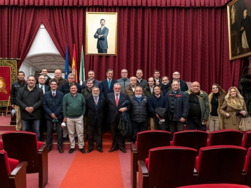 Reunión de autoridades en un salón con cortinas rojas y retratos enmarcados.