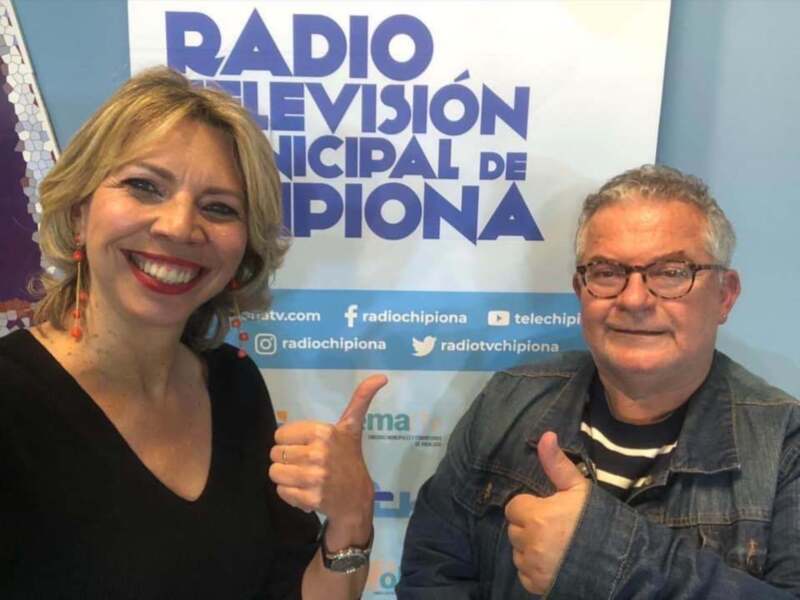 Dos personas sonrientes frente a una pancarta de Radio Municipal de Chivilcoy, mostrando un gesto de aprobación con los pulgares hacia arriba.