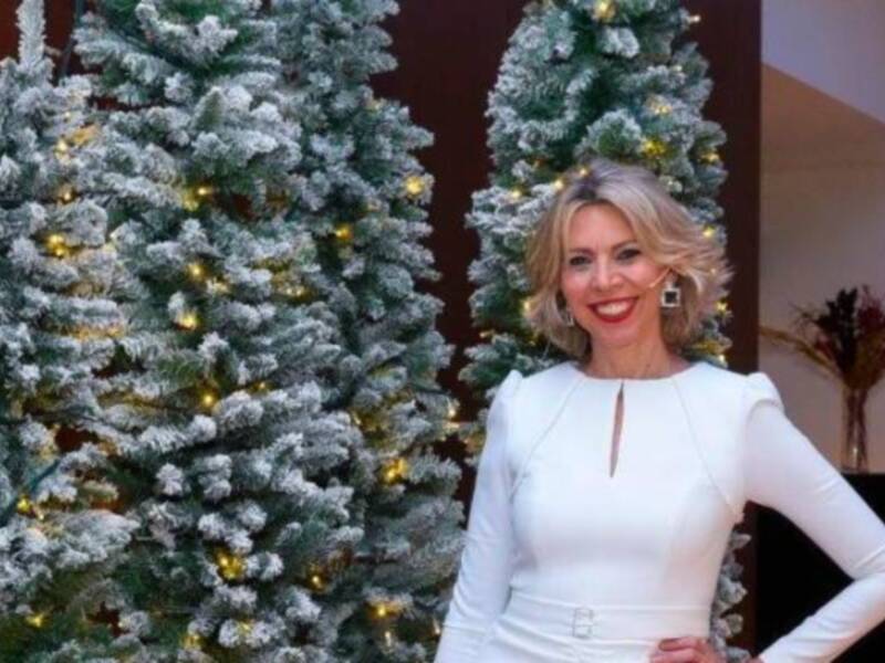 Una mujer sonríe en un ambiente navideño, rodeada de árboles de Navidad decorados con luces.