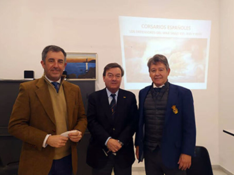 Tres hombres en trajes posan frente a una presentación sobre 'Los Corsarios Españoles' en un entorno profesional.